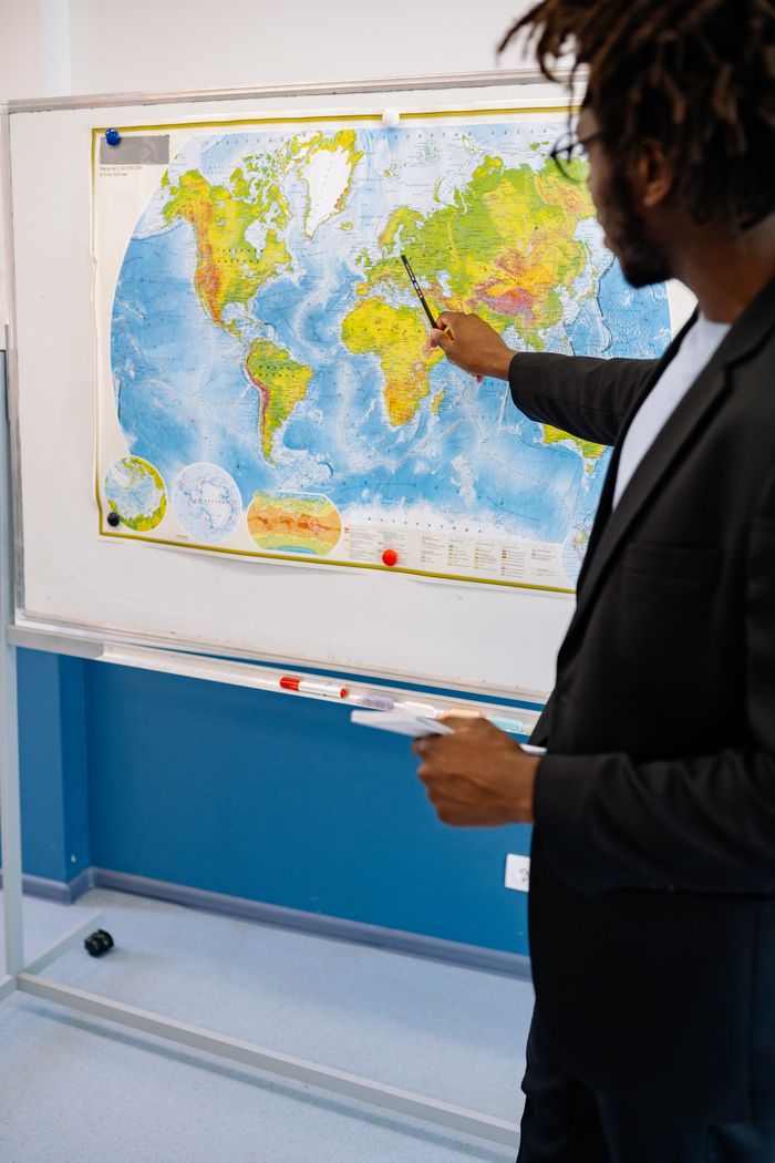 services-02 Teacher pointing at world map in classroom setting, emphasizing global geography.